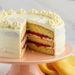 White chocolate raspberry cake on a light orange cake stand with a slice missing.
