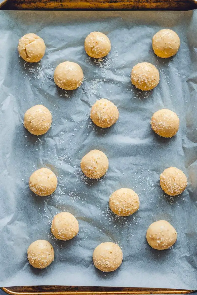 Sourdough sugar cookies dough balls sprinkled with granulated sugar and placed on a baking sheet.