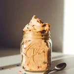 Rustic glass jar filled with creamy edible sugar cookie dough, sitting atop a simple white table.