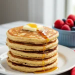 Eggless pancakes on a white plate with a pat of butter is melting on top and a light drizzle of maple syrup.