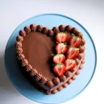 heart cake​ topped with strawberries and placed on a blue cake stand