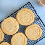 Top-down view of sourdough sugar cookies on a cooling rack against a light blue surface.