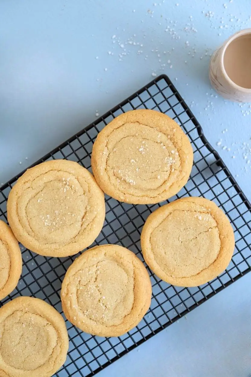 Top-down view of sourdough sugar cookies on a cooling rack against a light blue surface.