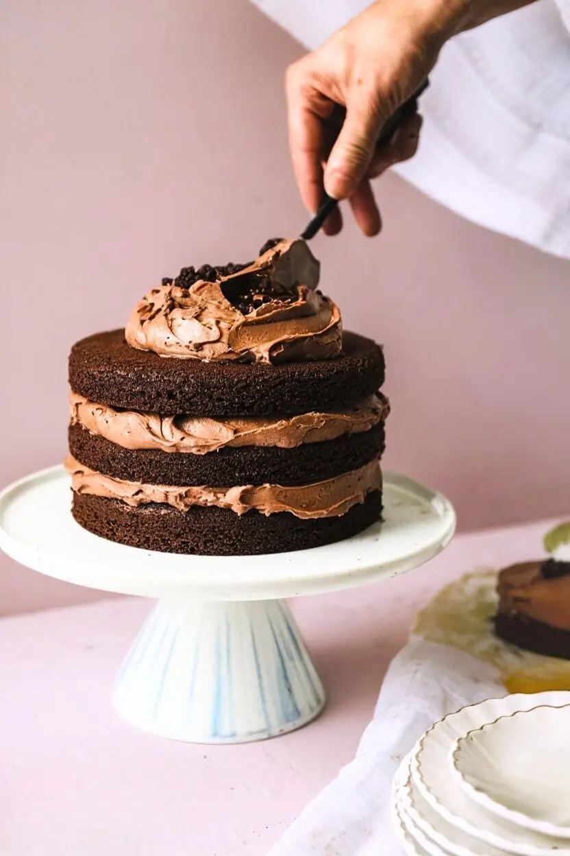 Three chocolate cakes on a cake stand with chocolate frosting between each layer.