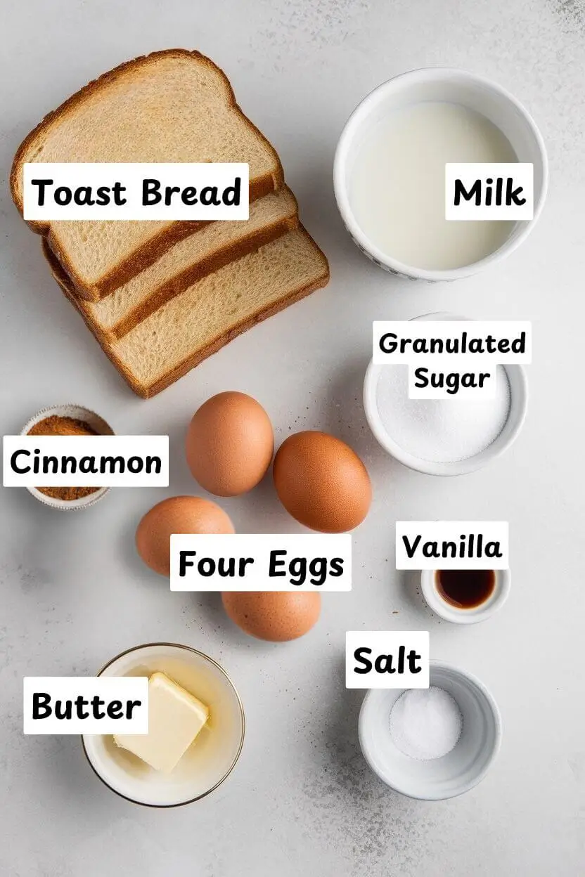 Ingredients on white table including toast bread, milk, sugar, eggs, cinnamon, vanilla, salt, and butter.